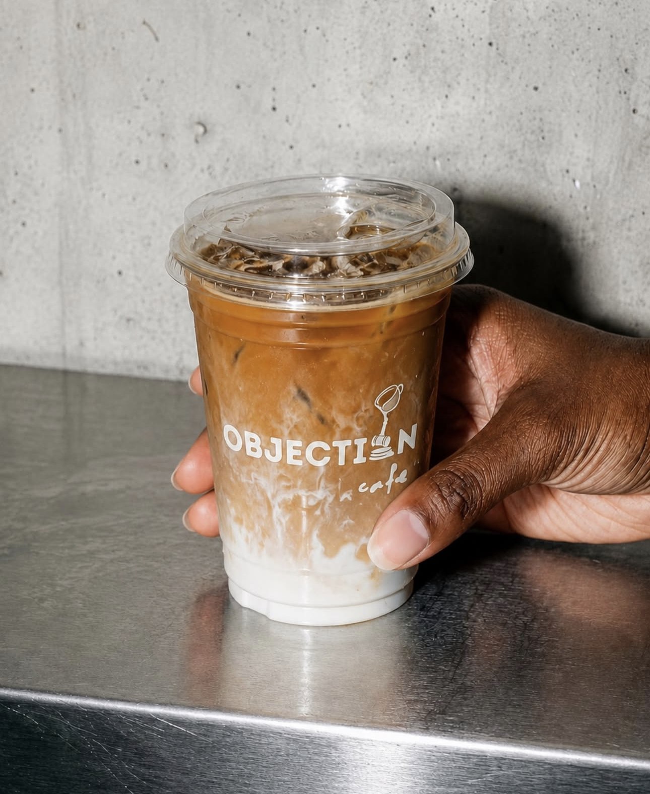Iced coffee in an Objection Cafe cup held against a concrete wall